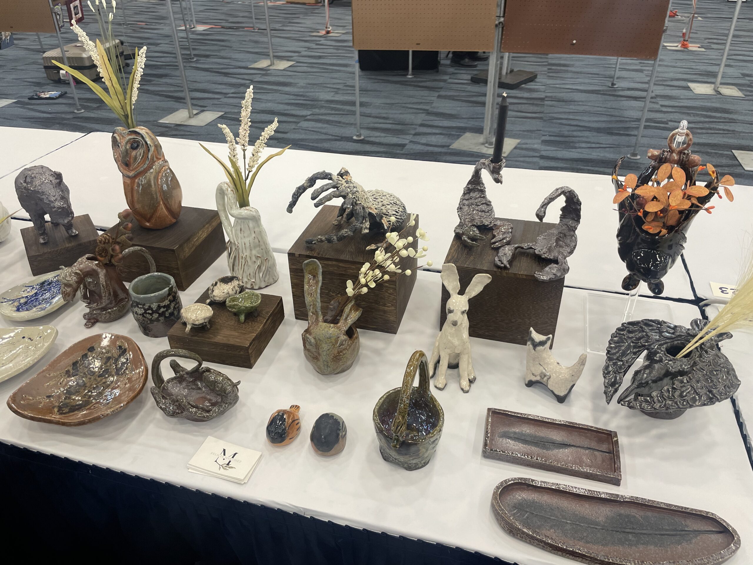 Display table with a variety of glazed ceramics: an owl vase, a white hare, two scorpions, a tarantula, a hanging bat vase, and several smaller delights.
